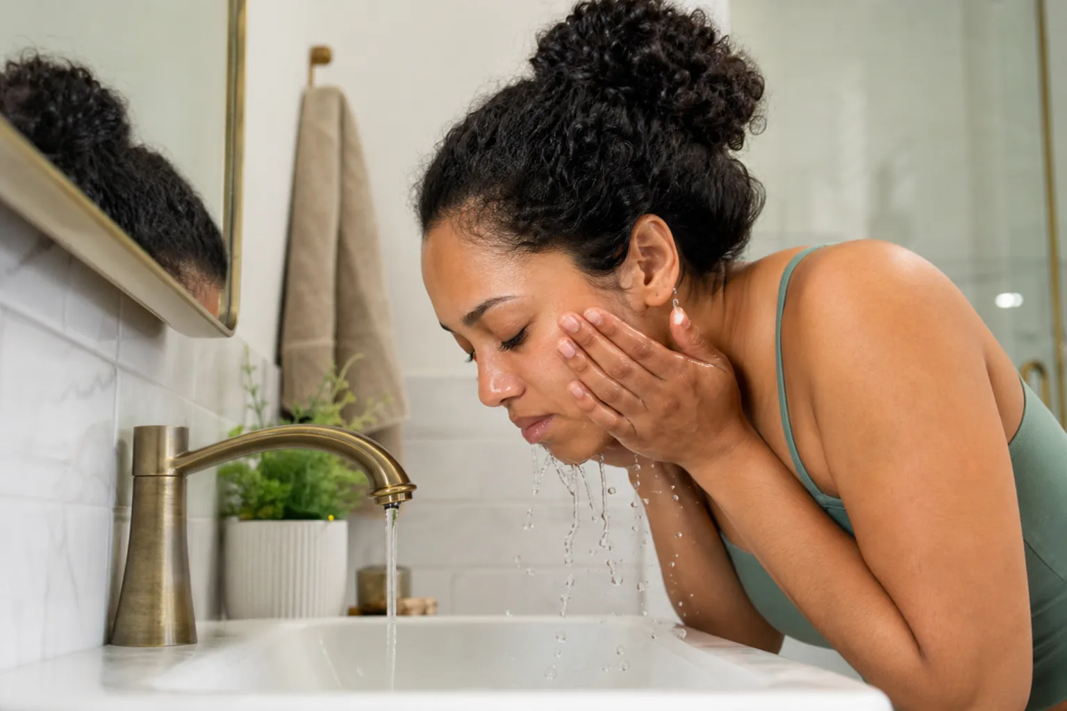 A person gently washing their face with fingertips and warm water in a bright bathroom.